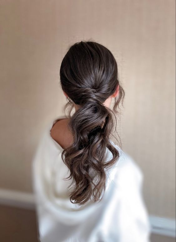 a dreamy wavy low ponytail with twisted hair and a sleek top plus locks framing the face is a lovely idea for a modern bride