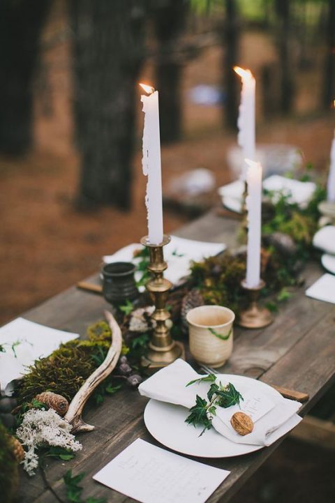 a fall woodland tablescape done with a moss runner, pinecones, antlers and nuts seems simple but also very chic