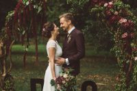 a fall woodland wedding arch of branches, with pink and burgundy blooms and lush greenery plus monograms is amazing