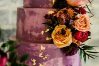 a fantastic mauve and plum-colored wedding cake with godl leaf, bright blooms and leaves is wow