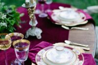 a gorgeous fall wedding tablescape with plum-colored velvet textiles, greenery, tall and thin candles and gold-rimmed glasses