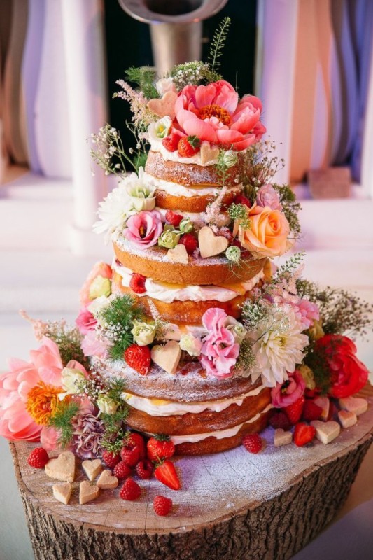 a gorgeous naked wedding cake decorated with hearts, strawberries, pink and white blooms and greenery is amazing for summer