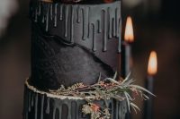 a haunted black wedding cake with black drip, herbs, greenery and dark blooms and macarons on top is a lovely idea for a Halloween wedding