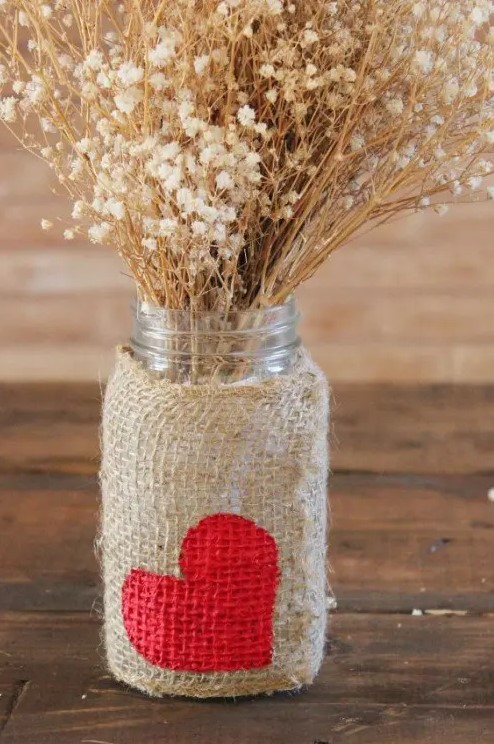 a jar with a burlap wrap with a heart and some dried blooms is a pretty rustic Valentine's Day centerpiece