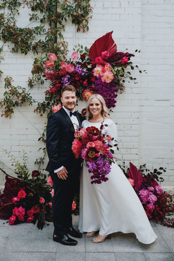 A jaw dropping wedding altar with fuchsia, pink, red and plum colored blooms and fronds is amazing for the fall