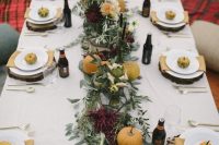 a laid-back fall wedding tablescape with a greenery, bloom and orange pumpkin table runner, wood slice placemats, beer bottles and neutral napkins