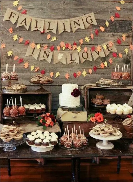 a large rustic dessert table of wood, with wooden crates and drawers, bright blooms, burlap and colorful leaf buntings and lots of food