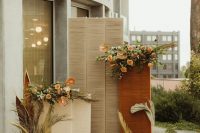 a lovely fall wedding backdrop of rattan, rust and blush blooms, greenery and pampas grass, candles and boho rugs is awesome