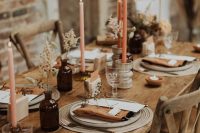 a lovely natural colored Thanksgiving tablescape with colored bottles, tall and thin candles, neutral chargers and plates