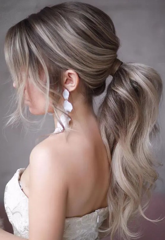 a lovely wavy and textural low ponytail with a bump on top and some locks framing the face is a chic idea to try