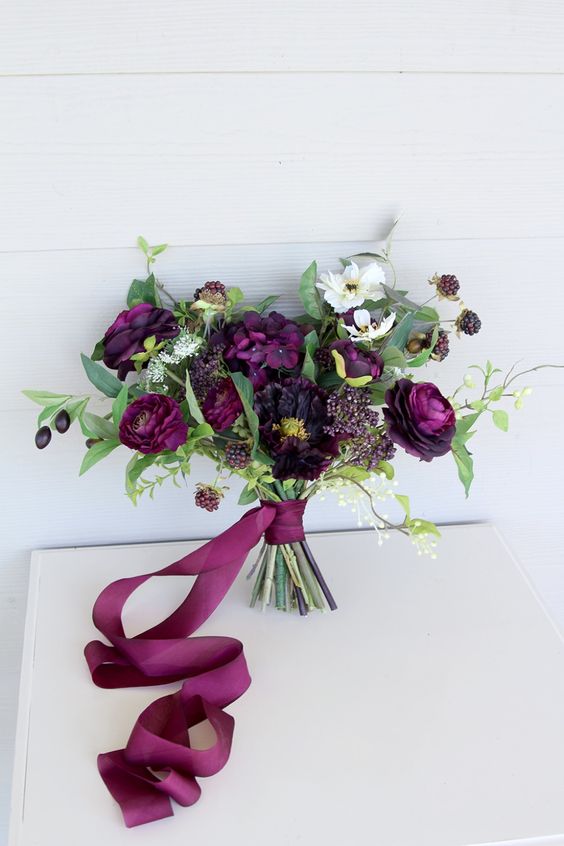 A lovely wedding bouquet with plum colored and white blooms, berries, greenery and plum colored ribbons is amazing