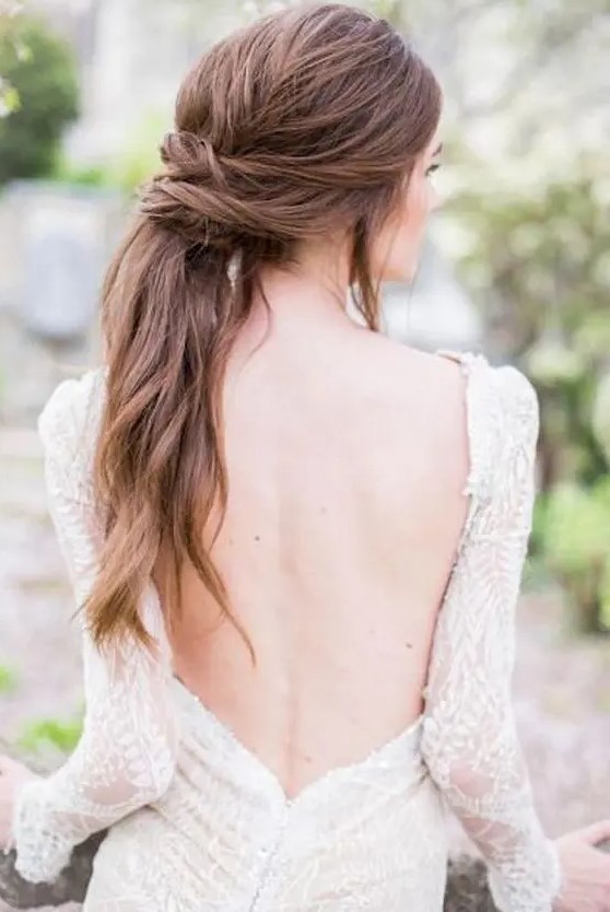 a low twisted and textural ponytail with some locks down and waves for an effortlessly chic look