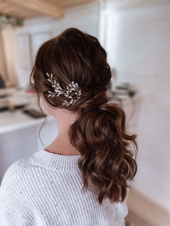 a low wavy ponytail with a twisted top and locks drown, with an embellished headpiece is a lovely idea