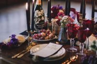 a lush decadent Halloween bridal shower tablescape with tall and thin black candles, gold cutlery, bold jewel-tone blooms and neutral ones, too
