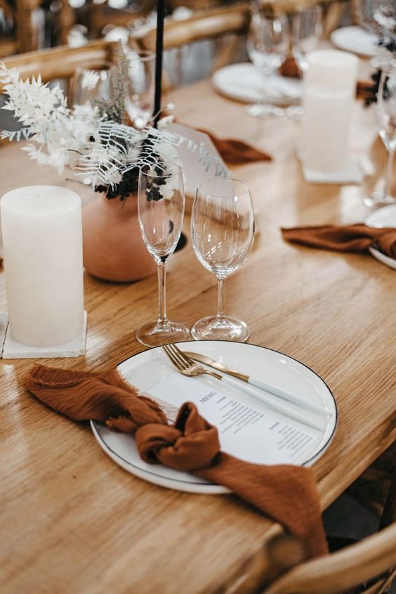 a minimalist Thanksgiving tablescape with pillar candles, terracotta vases and napkins, dried leaves and gold cutlery