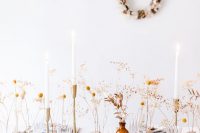 a neutral Thanksgiving table setting with dried leaves and flowers, tall and thin candles, gold cutlery and tree branches