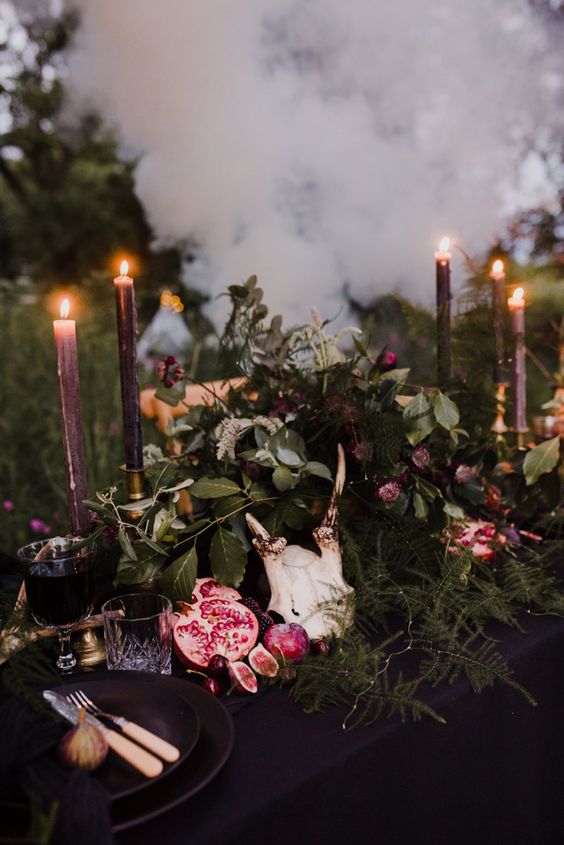 a pagan fall woodland wedding tablescape with much textural greenery, dark blooms, purple candles, fresh fruits for a decadent feel