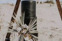 a plain black wedding cake decorated with lotus slices, blooms, twigs, pampas grass and some dried leaves is a gorgeous solution for a boho wedding in the desert