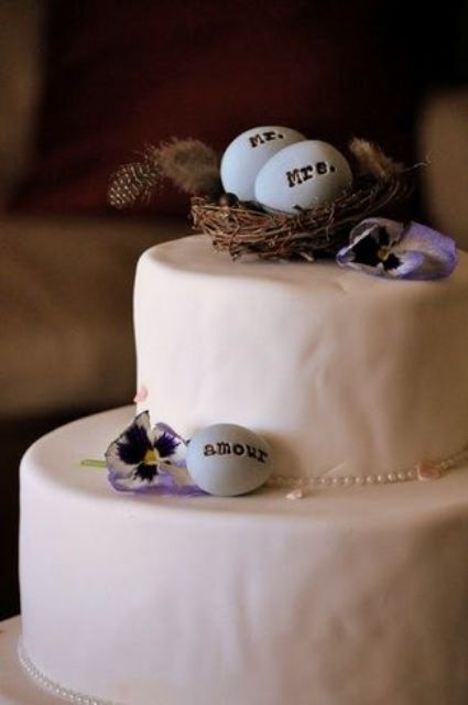 a plain white wedding cake topped with bold blooms, faux eggs, with a nest and feathers is a cool idea for a spring wedding