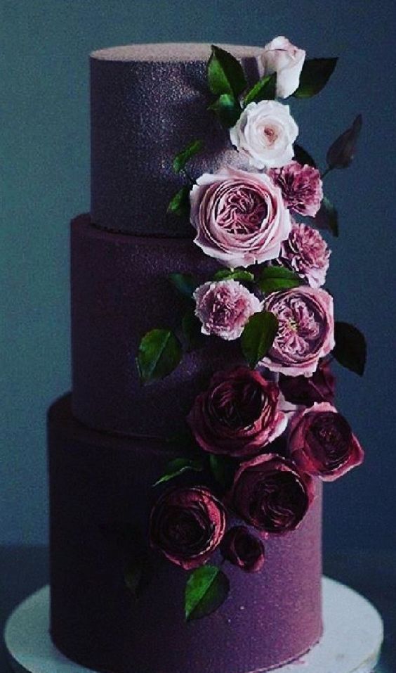 A plum colored textural wedding cake decorated with ombre blooms coming up from the bottom and some leaves is wow