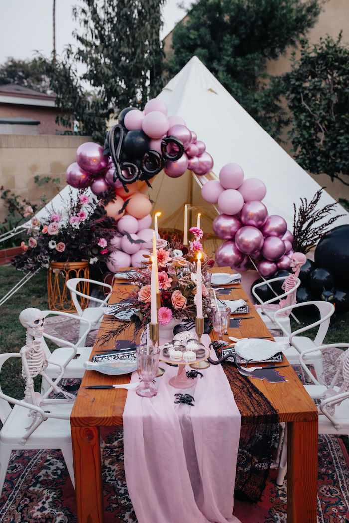 a pretty and bold Halloween bridal shower tablescape with pinks and black touches, with a lush floral centerpiece and a pink glassware