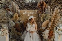 a pretty boho wedding backdrop of burlap, a neon sign and colored dried fronds and pampas grass is amazing
