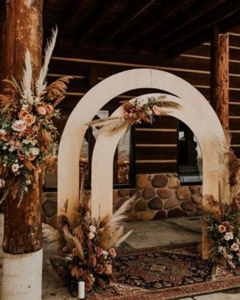 a pretty boho wedding backdrop of two plywood arches, pampas grass, peastel and rust blooms and a boho rug on the floor