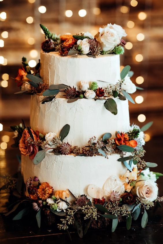 a pretty fall woodland wedding cake with greenery, blush and rust looms, foliage and other stuff is amazing