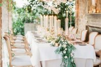 a refined Tuscany wedding reception with tall candles, greenery and white blooms and candles on the floor