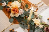 a refined and chic Thanksgiving tablescape with a rust table runner, pastel and rust blooms, candles, white plates and gold cutlery