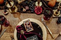 a refined decadent Halloween bridal shower tablescape with gld empty frames, lush jewel-tone blooms, tall black candles and velvet blood-colroed napkins