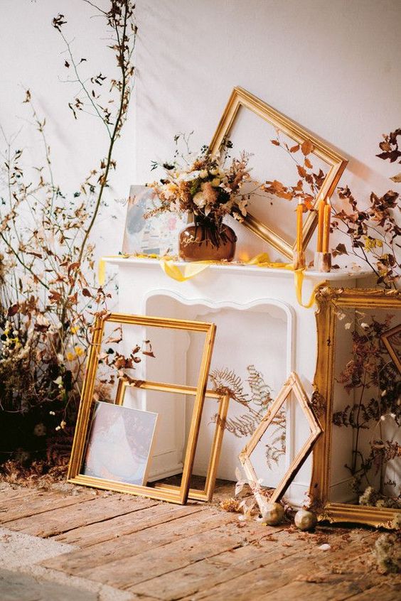 a refined fall wedding backdrop of a faux fireplace, empty frames, fall leaves, candles and a floral arrangement is a gorgeous idea