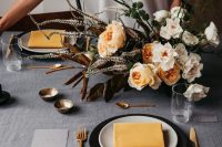 a refined modern Thanksgiving tablescape with a grey linen tablecloth, black and white plates, yellow napkins, a bold dimensional floral arrangement