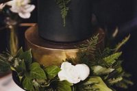 a refined wedding cake with a black and gold tier, greenery and foliage and white blooms on top is a fantastic idea for a modern wedding