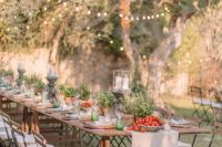 a relaxed Tuscany wedding tablescape accented with potted greenery, with peppers and tomatoes in bowls and pillar candles