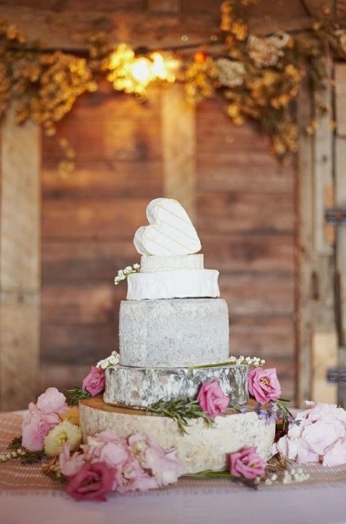 a romantic cheese wheel wedding cake topped with a heart shaped cheese piece and decorated with pink roses for a rustic wedding