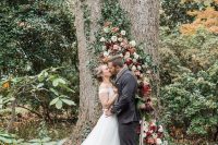 a romantic fall woodland wedding backdrop of a living tree decorated with blush and deep red blooms and greenery