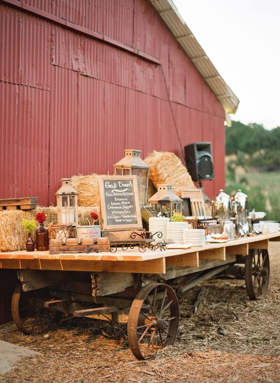 a rustic dessert table of a large cart, hay, bright blooms, candle lanterns and plates and mugs