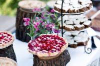 a rustic dessert table styled with tree stumps, a rustic stand with a metal handle and bright blooms in bottles