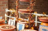 a rustic fall dessert table with a metal pie stand decorated with berries and leaves, wood and wicker stands, letters, pinecones and acorns