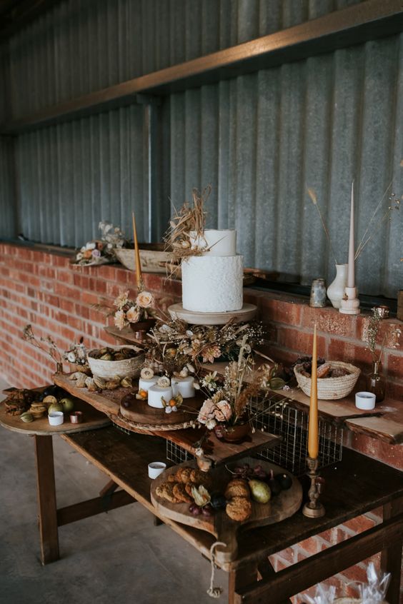 a rustic fall dessert table with wooden cutting boards, stands, dried blooms and leaves and mustard candles