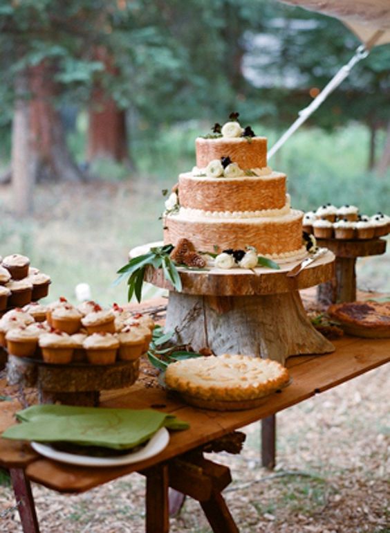 a rustic sweets table with tree slices and tree stumps, greenery, pinecones and lots of delicious sweets
