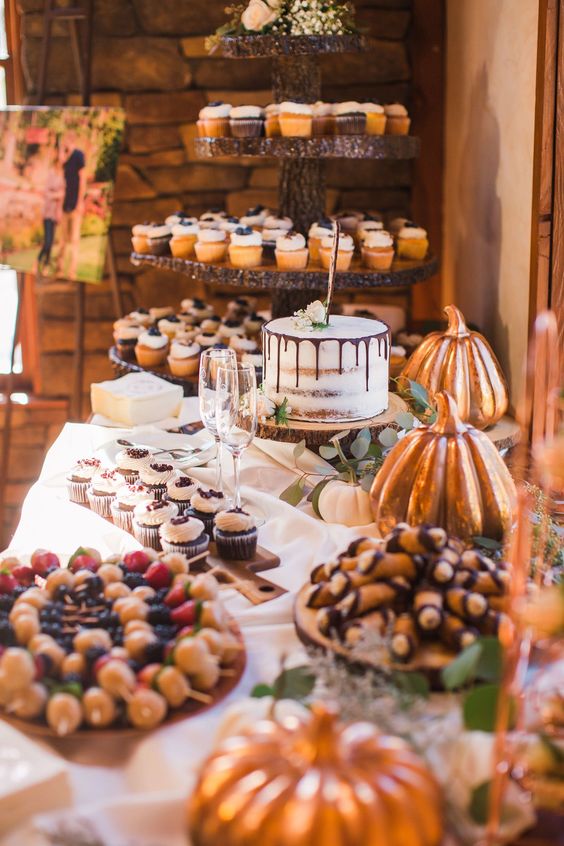 a rustic sweets table with tree slices for serving food, wood cutting boards, tree slice stands with sweets and leaves and pumpkins