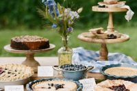 a rustic vintage dessert table with wooden stands, cowls with pies, wildflowers, floral anpkins and berries in a bowl