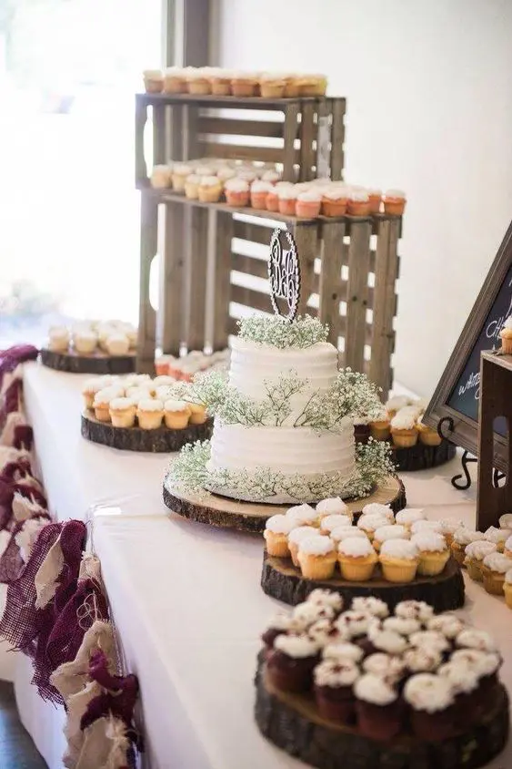 a simple rustic sweets table with tree slices, crates and a fabric garland is a cool option
