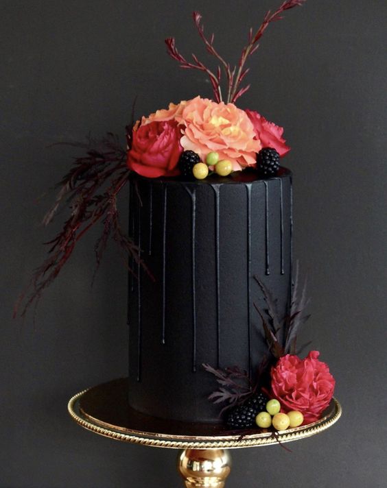 a small matte black wedding cake with black drip, berries, red and pink blooms, feathers and twigs is a beautiful and modern idea to rock