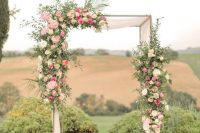 a sophisticated wedding ceremony arch decorated with greenery, neutral and pink blooms and oversized candle lanterns
