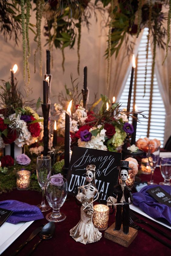 a super bold Halloween bridal shower tablescape with jewel-tone florals, black tall and thin candles, purple napkins, black cutlery and greenery over the table