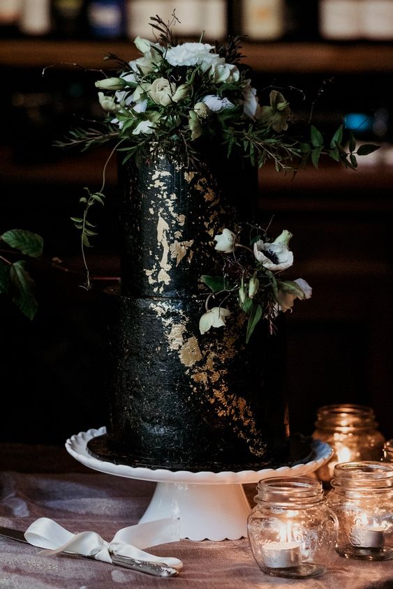 a textural black wedding cake with gold leaf, white blooms and greenery is a timeless idea for a fall or Halloween wedding