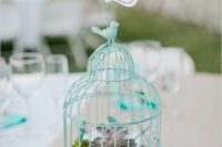 a turquoise cage with moss and succulents inside, with a turquoise love bird and a table number doubles a sa centerpiece